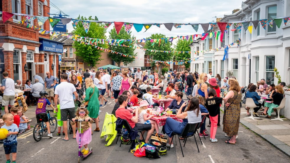 A street party taking place with crowds of people and colorful bunting tied between buildings